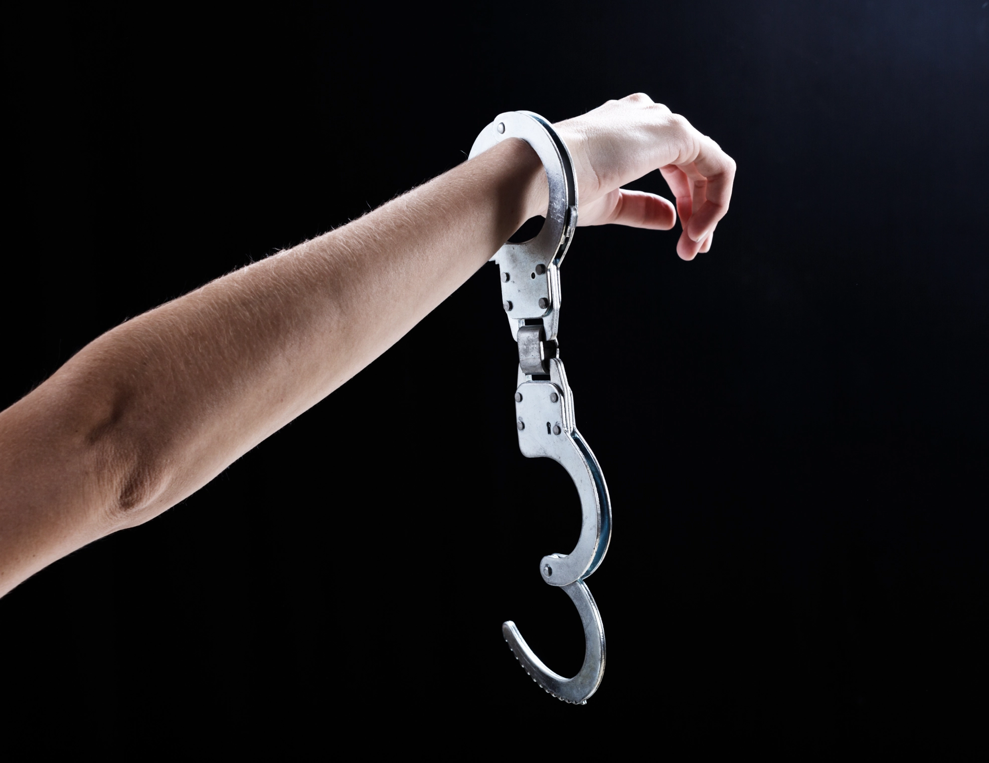 Arm with open handcuff against dark background.